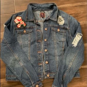 A blue jean jacket with rips and a rose pattern